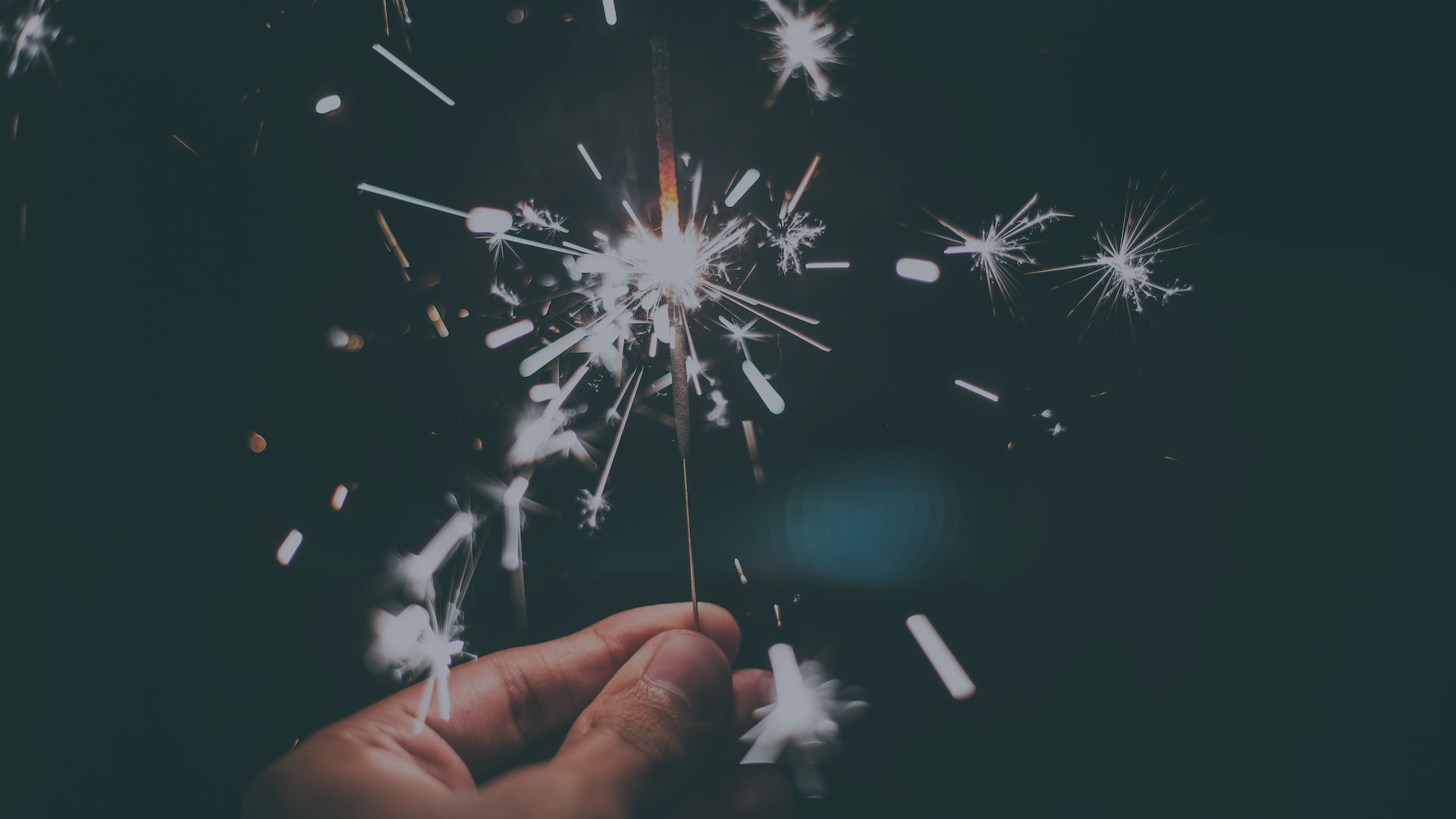 Hand holding a lit sparkler against a dark background, symbolizing new goals and business inspiration