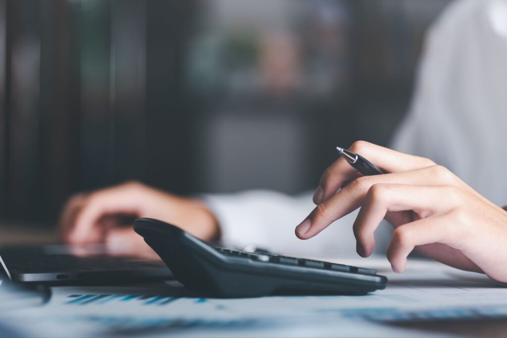 Close-up of a hand using a calculator on top of financial documents, representing the careful financial calculation and planning involved in securing bridge financing.